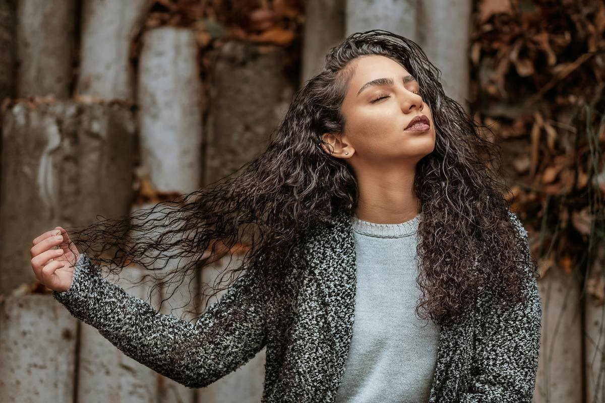 Black woman using a wide-tooth hair pick as a detangler for curls on wet, conditioned hair